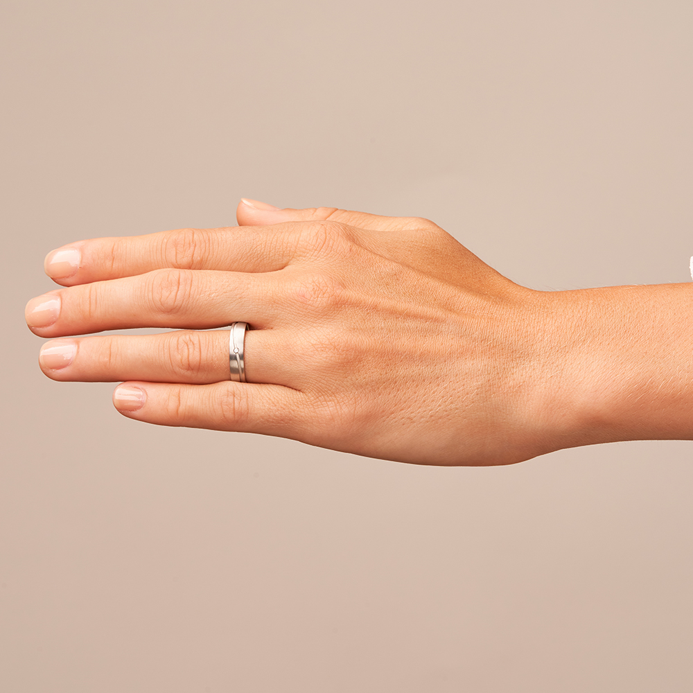 Längmattierte Weissgold Trauringe mit Diamanten in gewellter sandmatter Rille auf Hand