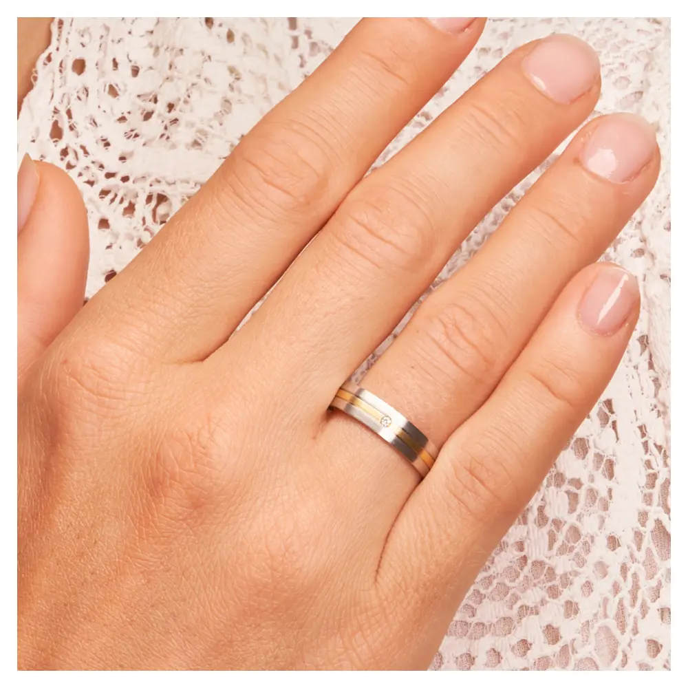 Weißgold und Gelbgold Eheringe längsmattiert mit Diamanten auf Hand am Gesicht im Zoom