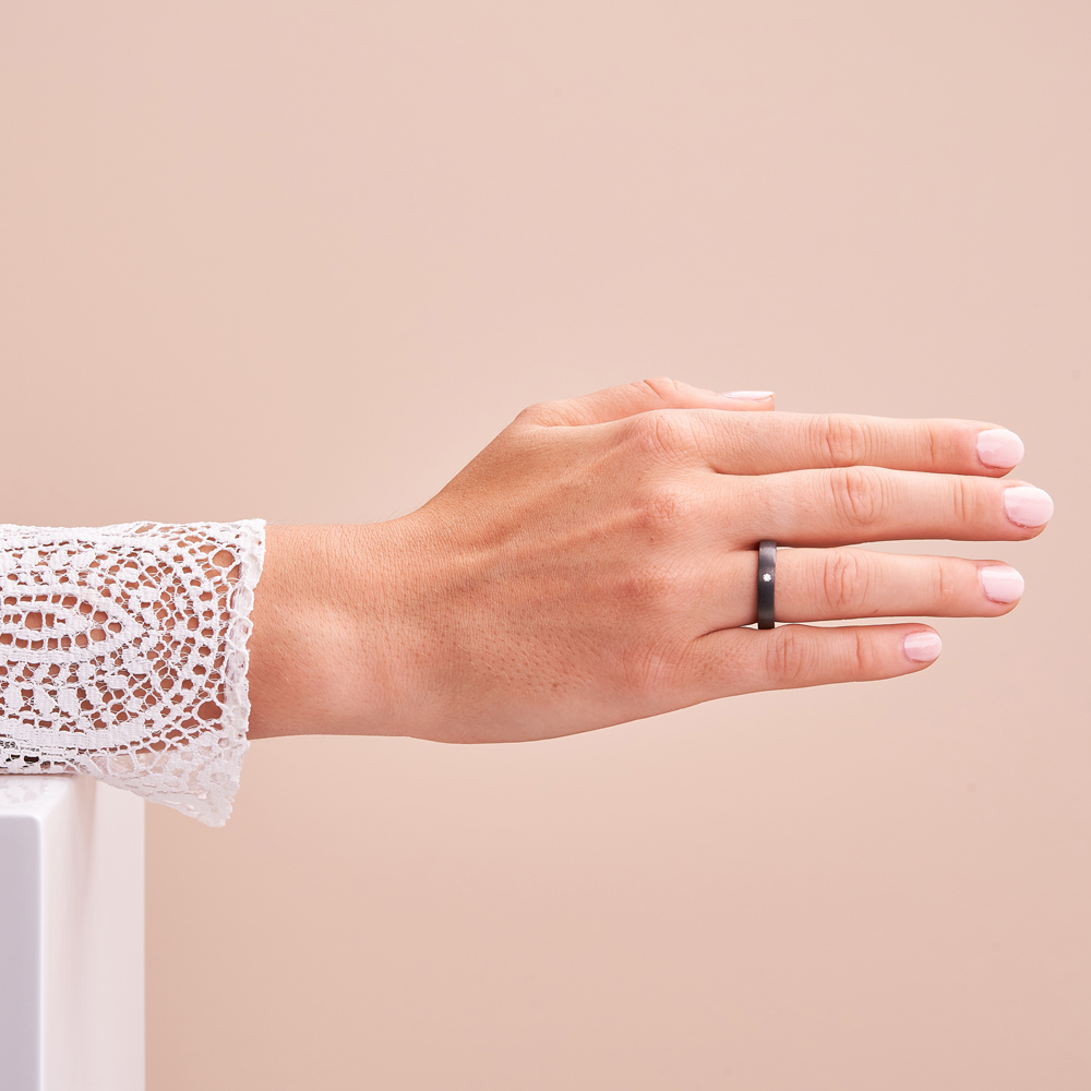 Aufnahme von schmalem Verlobungsring aus Carbon & Titan mit weißem Diamanten auf Hand