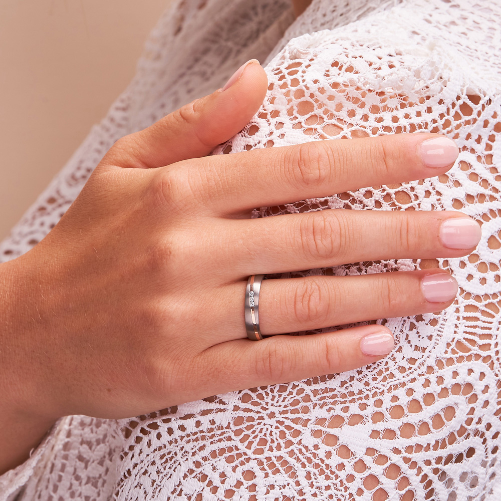 Aufnahme von Titan und Roségold Trauringen mit Diamanten in Kanalfassung auf Hand
