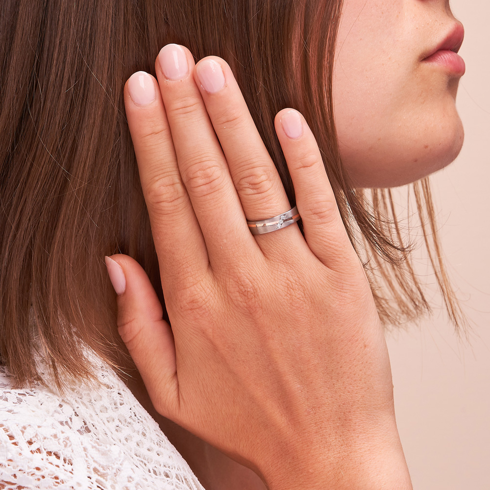 Aufnahme von Titan & Roségold Trauringen mit drei Diamanten in schräger Rille auf Hand