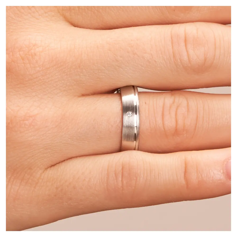 Trauringe aus platiniertem Silber 925 mit Diamanten und seitlicher Rille auf Hand im Zoom