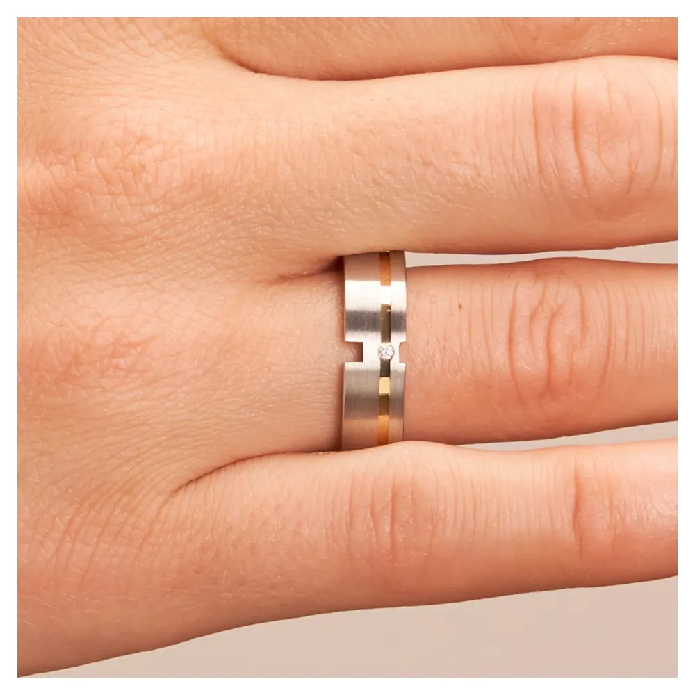Trauringe aus platiniertem Silber mit Gelbgoldstreifen mit Diamanten auf Hand im Zoom