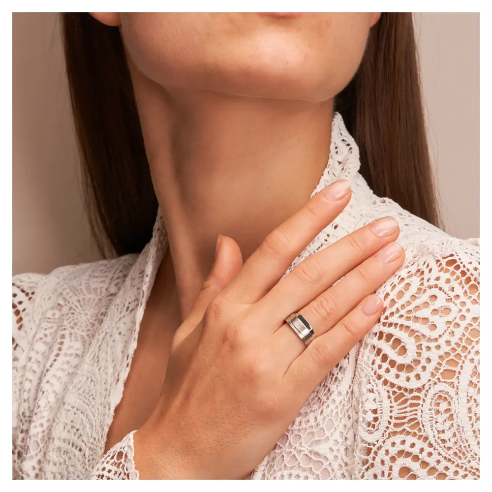 Asymmetrische Eheringe aus platiniertem Silber mattiert mit Diamanten auf Hand im Gesicht