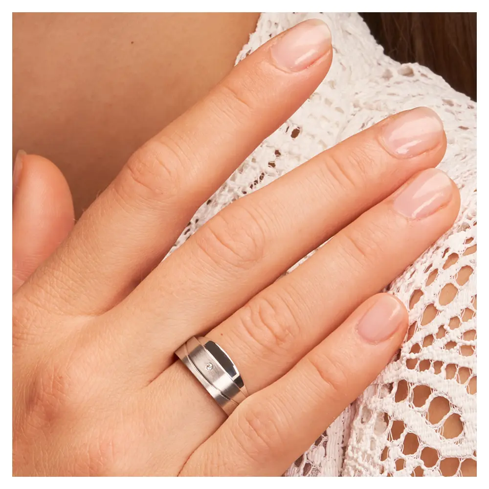 Asymmetrische Eheringe aus platiniertem Silber mattiert mit Diamanten auf Hand im Gesicht im Zoom