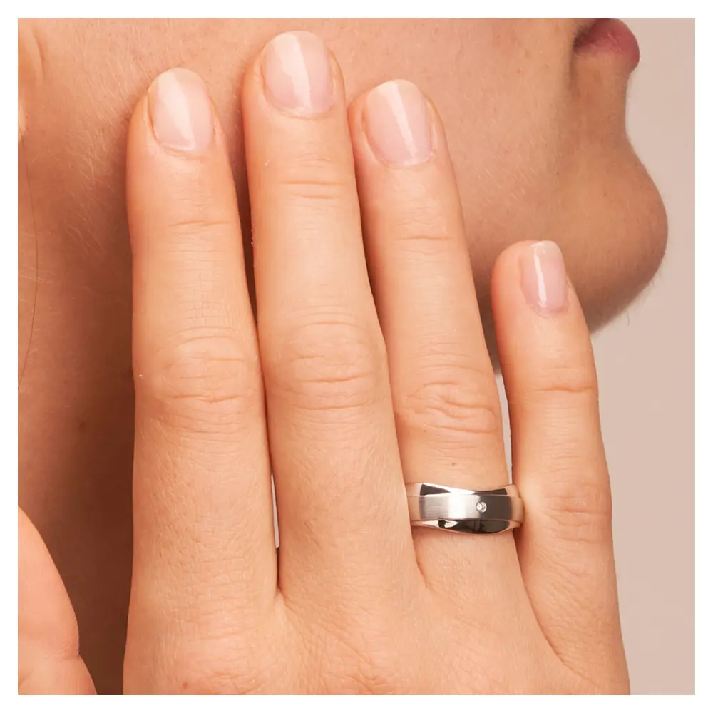 Trauringe aus Silber 925 platiniert mit welligem Rand und Diamant auf Hand am Gesicht im Zoom