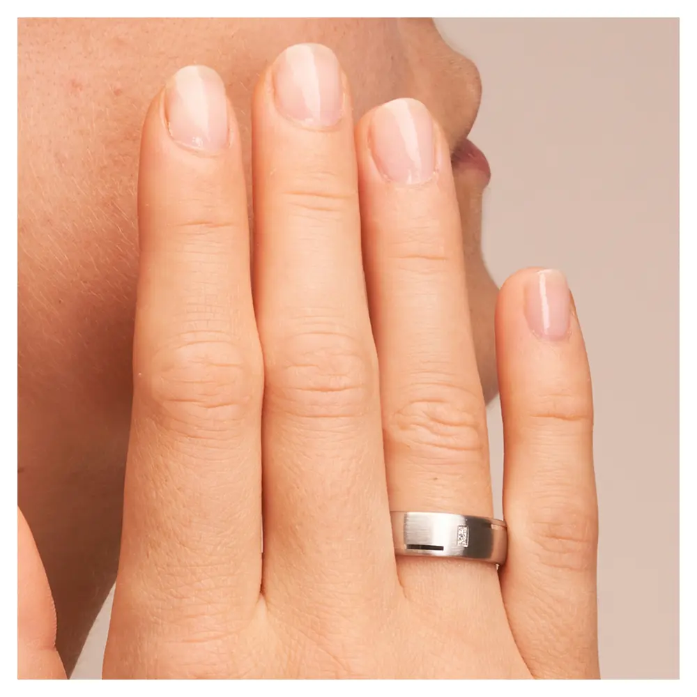 Matte Eheringe aus platiniertem Silber 925 mit zwei Diamanten und Rillen auf Hand am Gesicht im Zoom