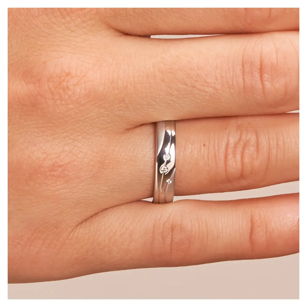 Trauringe aus platiniertem Silber 925 mit drei Diamanten und geschwungenen Rillen auf Hand im Zoom