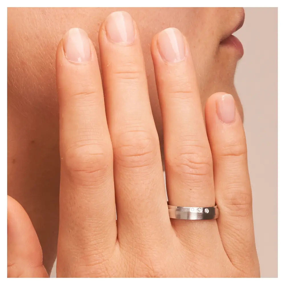 Eheringe aus Silber platiniert 925 strukturiert mit drei Diamanten auf Hand am Gesicht im Zoom