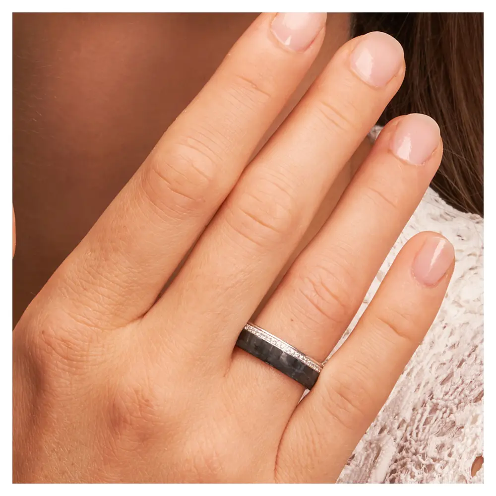Eheringe aus poliertem Platin und mattem Carbon mit Diamantenband auf Hand am Gesicht im Zoom