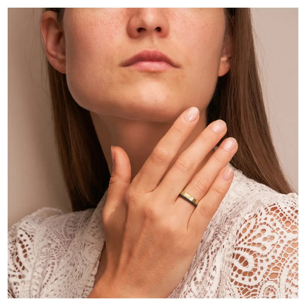 Eheringe aus Gelbgold mit Carbonstreifen und Diamanten auf Hand im Gesicht