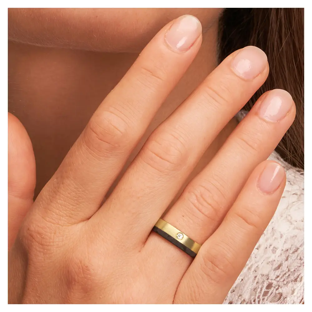 Eheringe aus Gelbgold mit Carbonstreifen und Diamanten auf Hand im Gesicht im Zoom