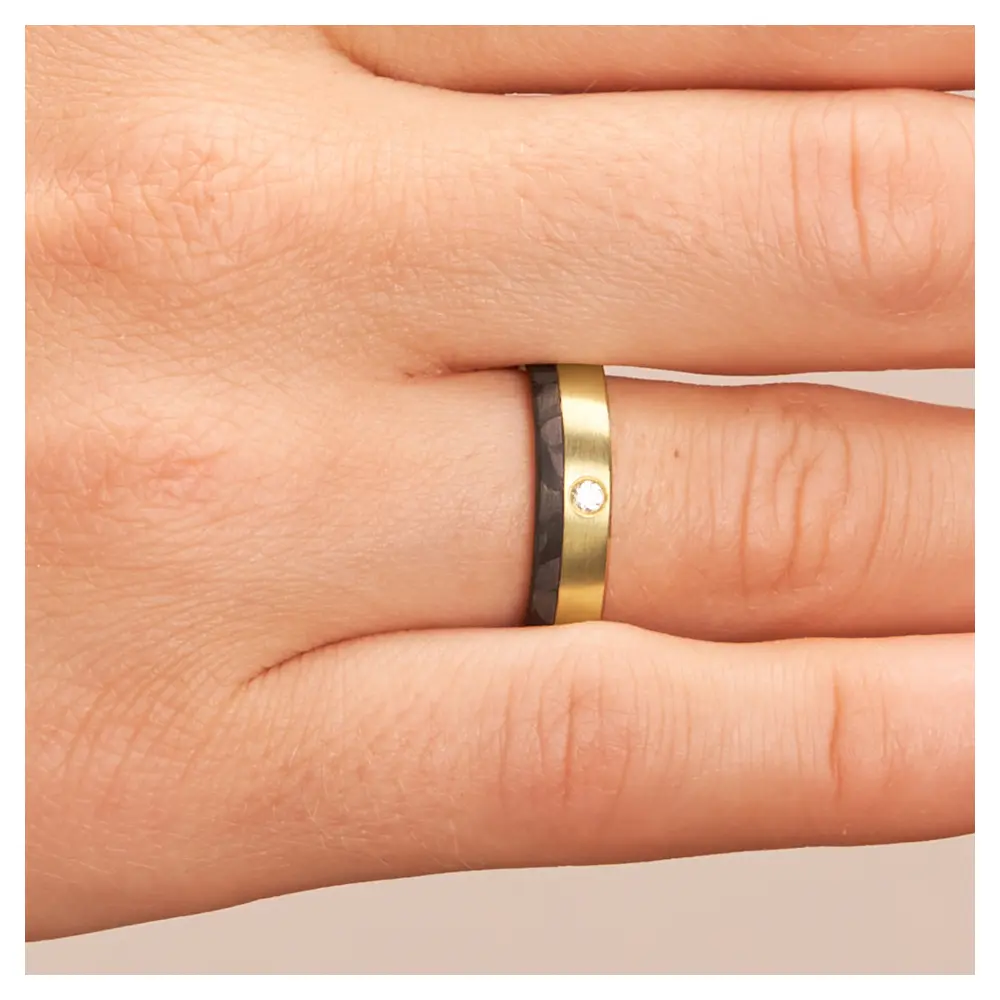 Eheringe aus Gelbgold mit Carbonstreifen und Diamanten auf Hand im Zoom