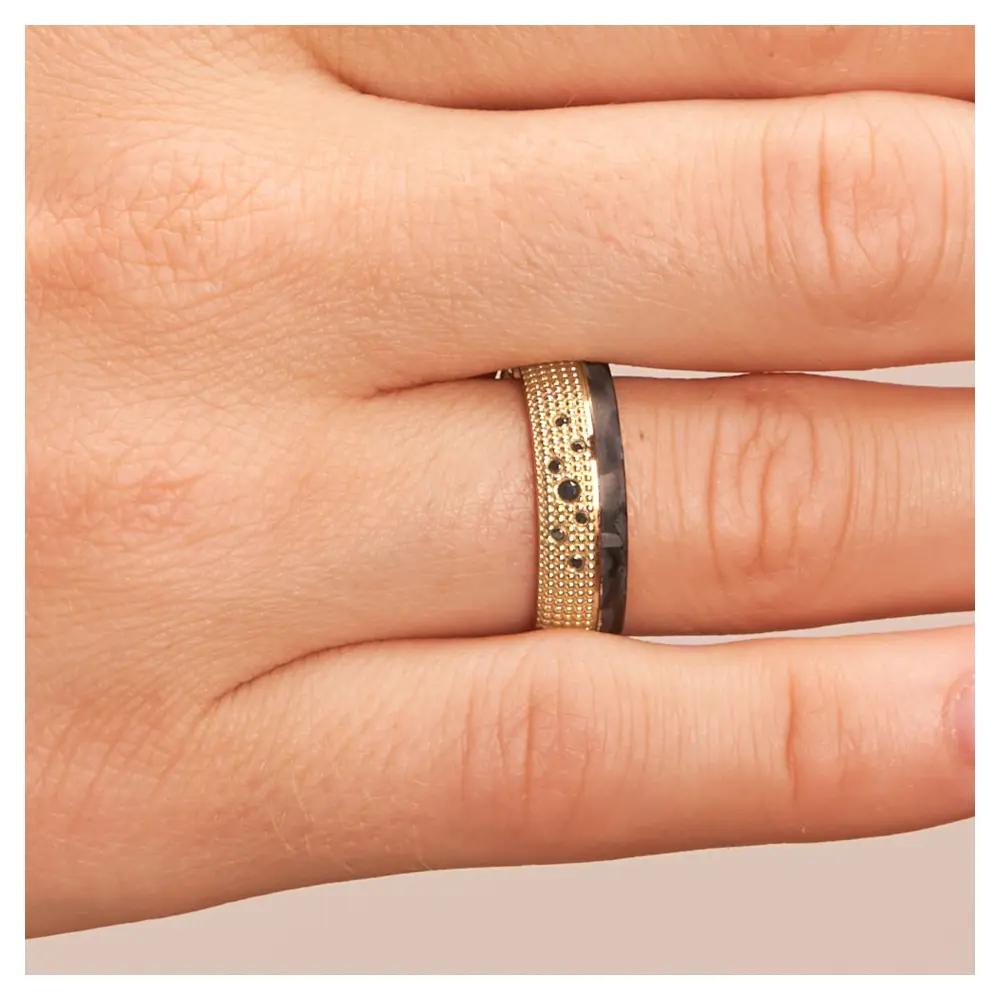 Eheringe aus Gelbgold und gemasertem Carbon mit schwarzen Diamanten auf Hand im Zoom