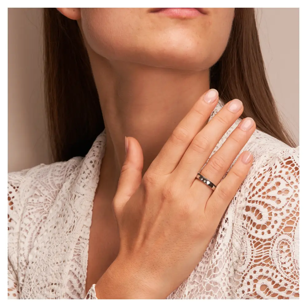 Polierte Eheringe aus Platin und Carbon mit seitlichem Muster und Diamanten auf Hand am Gesicht