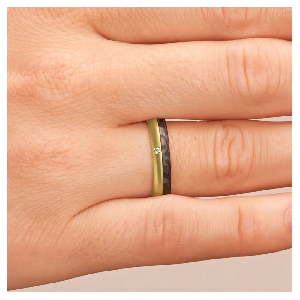 Eheringe aus Gelbgold und Carbon mit Diamanten und Querbürstung auf Hand im Zoom