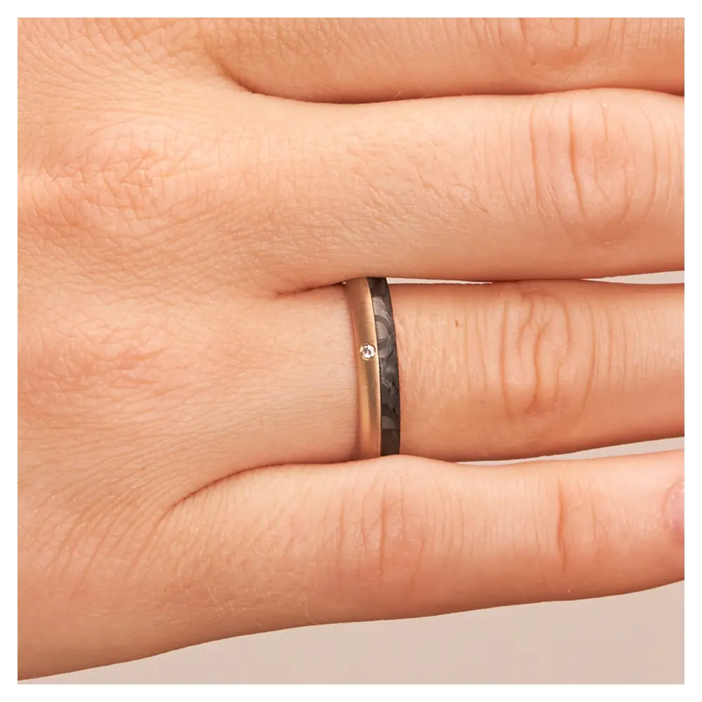Eheringe aus Rotgold und Carbon mit Diamanten und Querbürstung auf Hand im Zoom