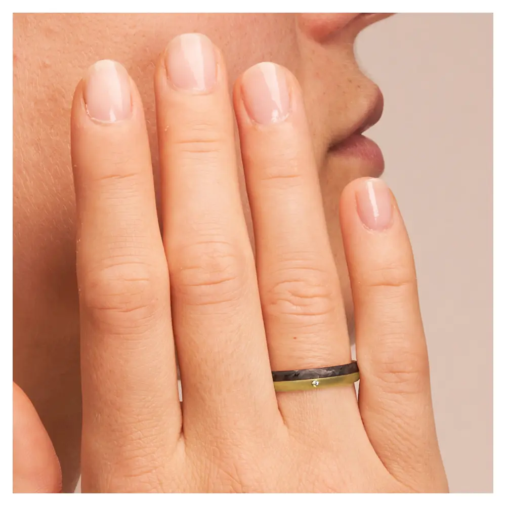Eheringe aus Gelbgold und Carbon mit Diamanten und Querbürstung auf Hand am Gesicht im Zoom