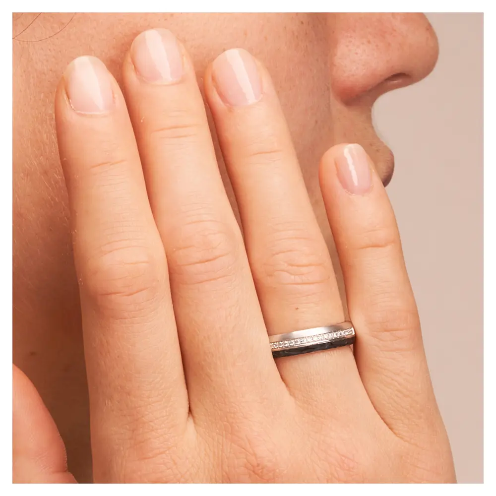Eheringe aus Platin mit Carbonstreifen und 20 Diamanten in Kanalfassung auf Hand am Gesicht im Zoom