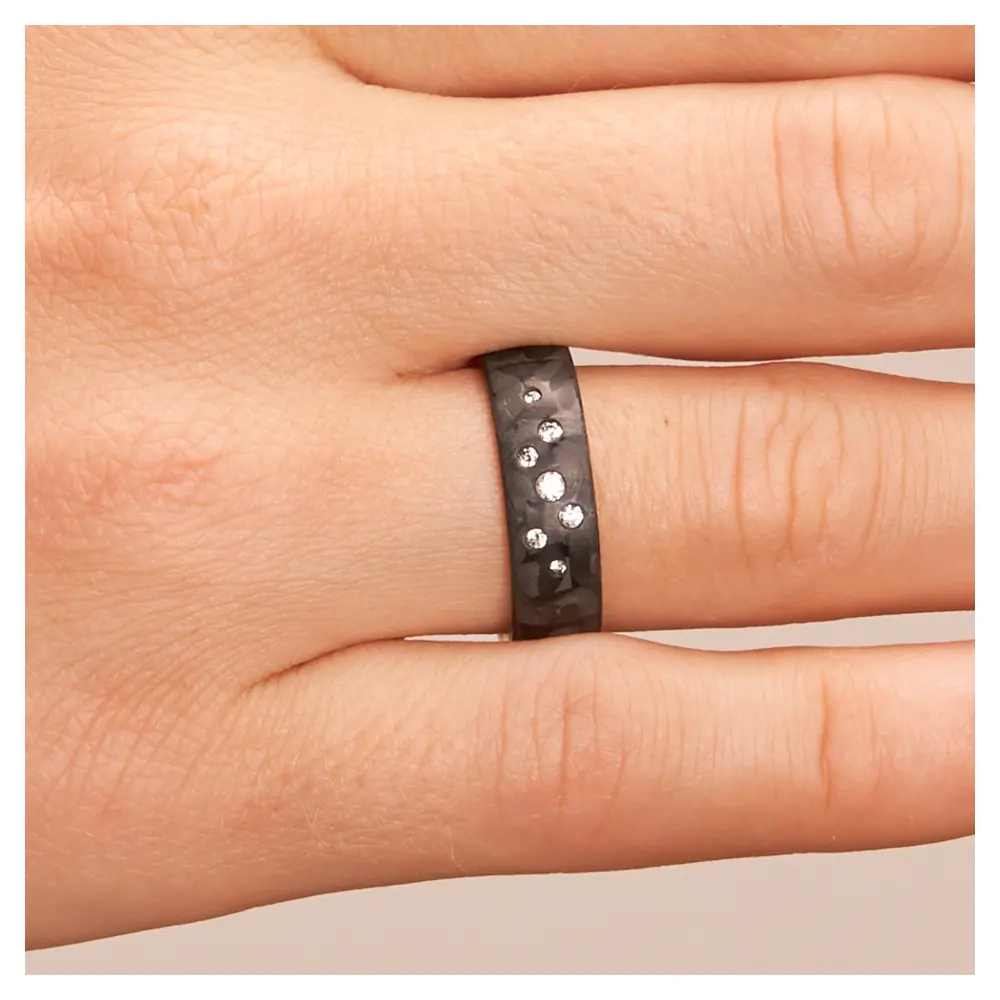Eheringe aus Weißgold und Carbon mit Diamanten als Sternenhimmel auf Hand im Zoom
