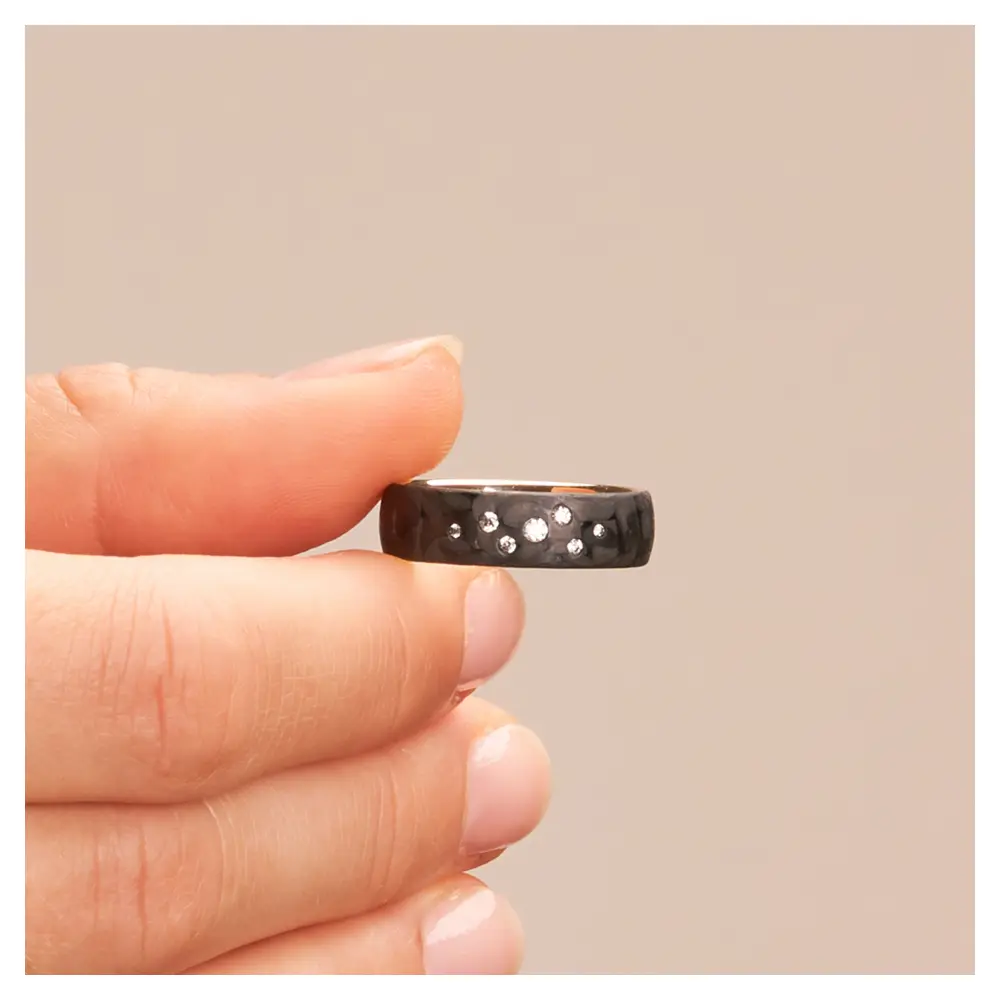 Eheringe aus Weißgold und Carbon mit Diamanten als Sternenhimmel in Hand