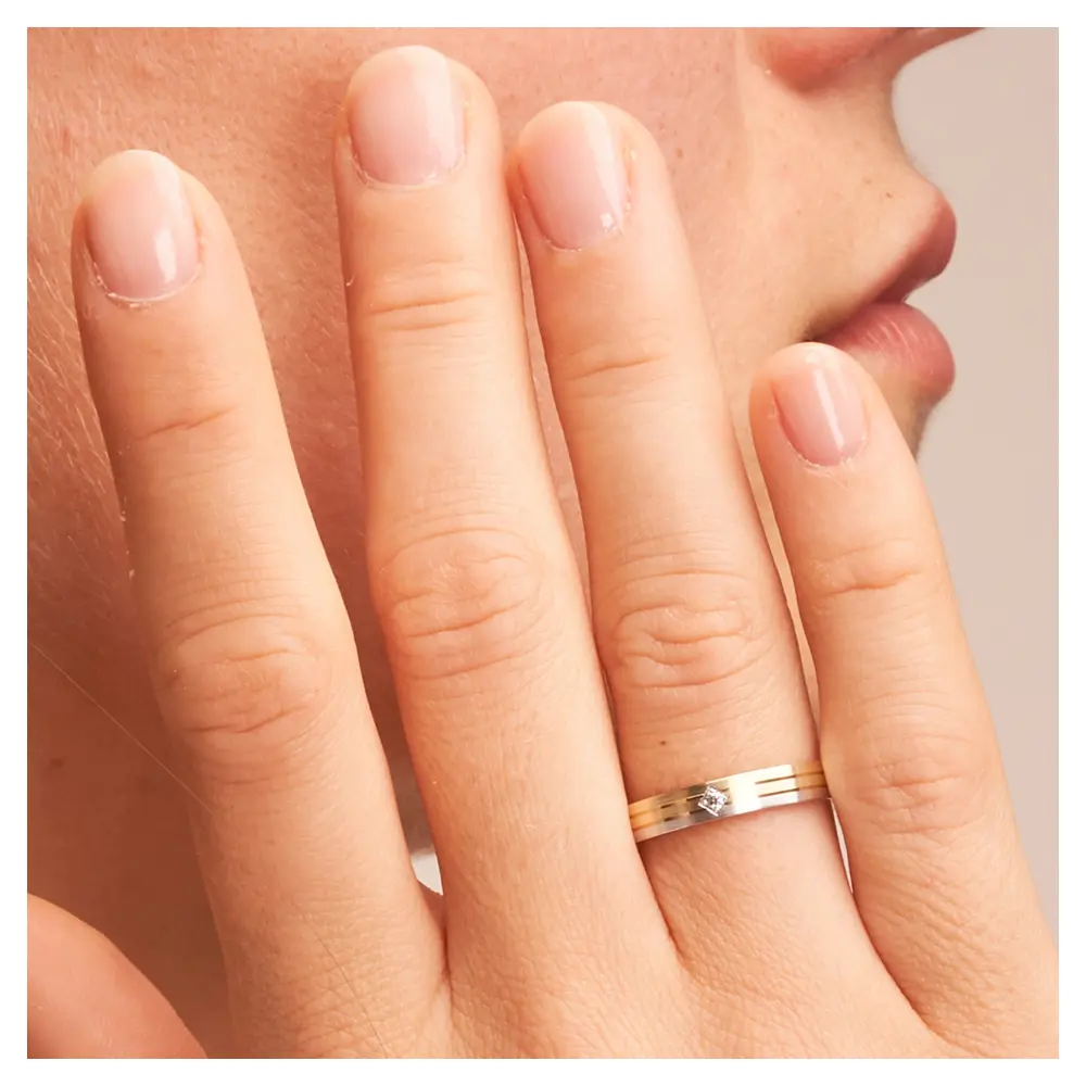 Trauringe aus Gelbgold und Weißgold schmal längsmatt mit Diamant auf Hand im Zoom
