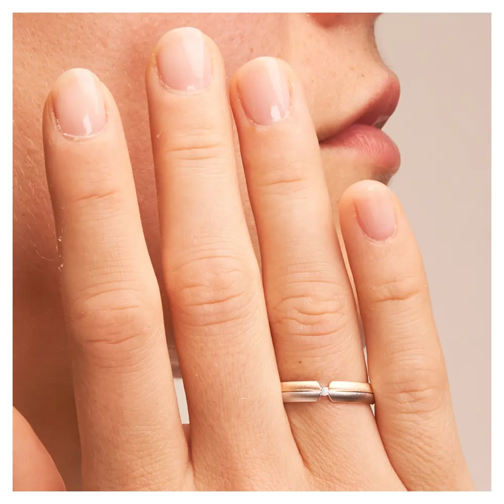 Trauring aus Weißgold und Roségold quergebürstet mit Diamant in Spannfassung auf Hand im Zoom