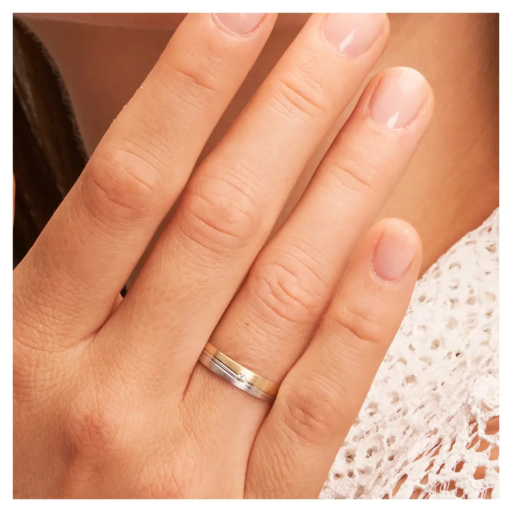 Trauringe aus Gelbgold und Weißgold mit Mattierung 2 schrägen Rillen und Diamant auf Hand im Zoom