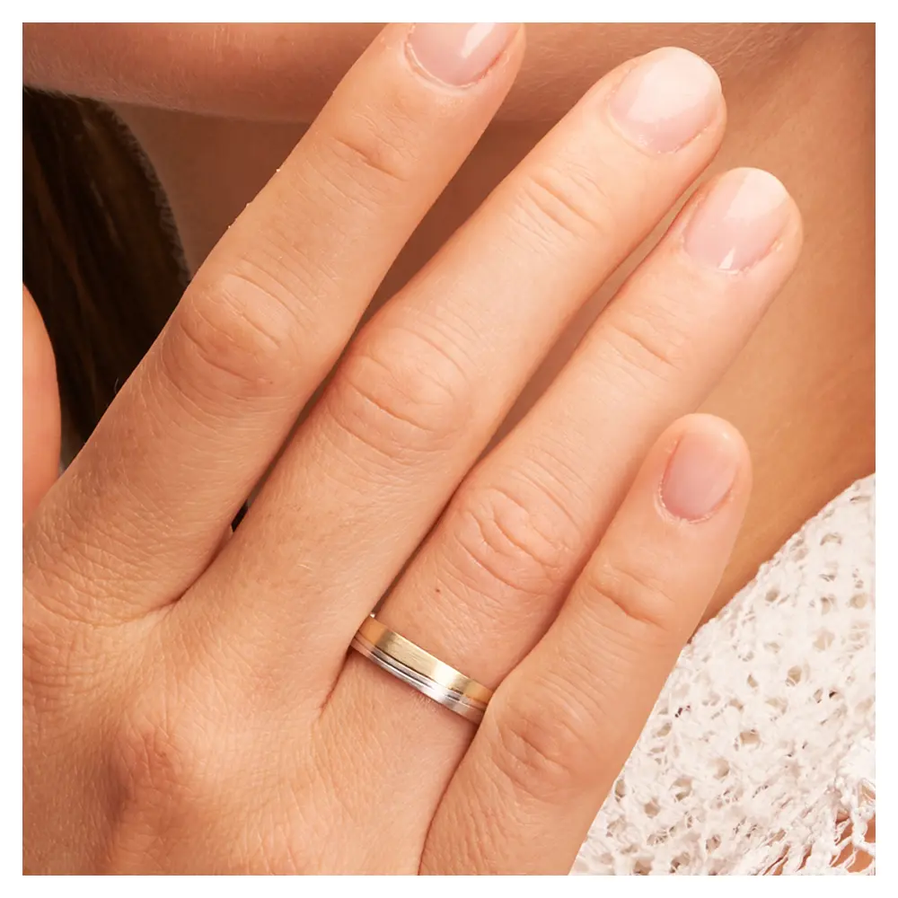Trauringe aus Gelbgold und Weißgold mit Mattierung und 2 schrägen Rillen auf Hand im Zoom