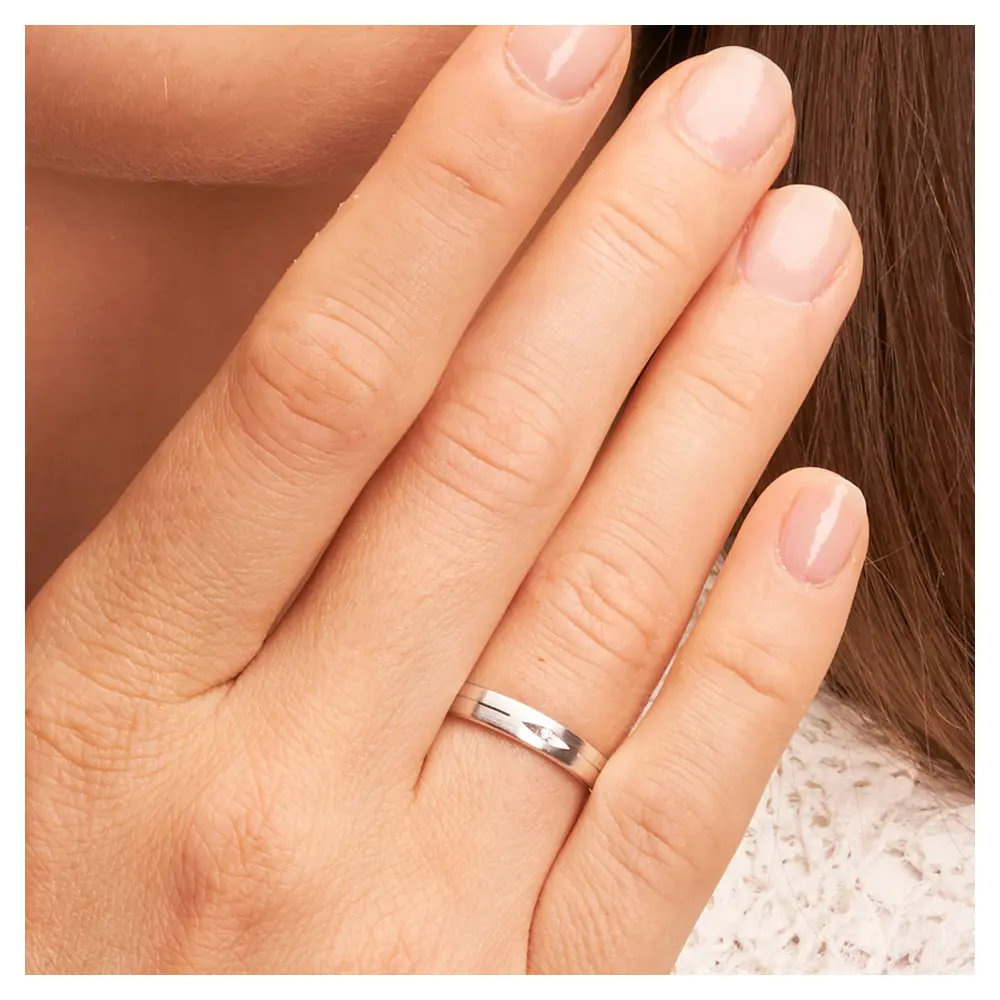 Mattierte Eheringe aus Weißgold mit Diamanten in augenförmiger Kerbe auf Hand im Zoom