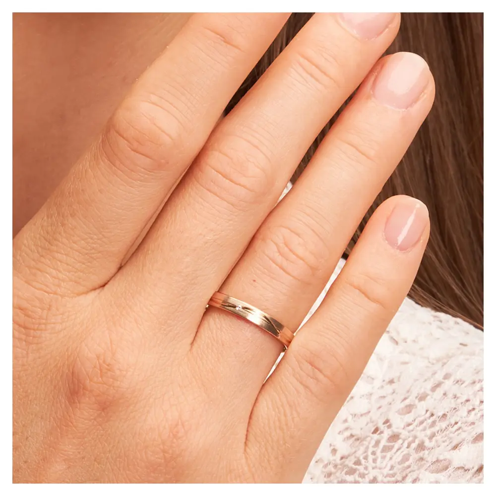 Trauringe aus Roségold mit Mattierung und geschwungenen Rillen und Diamant auf Hand im Zoom