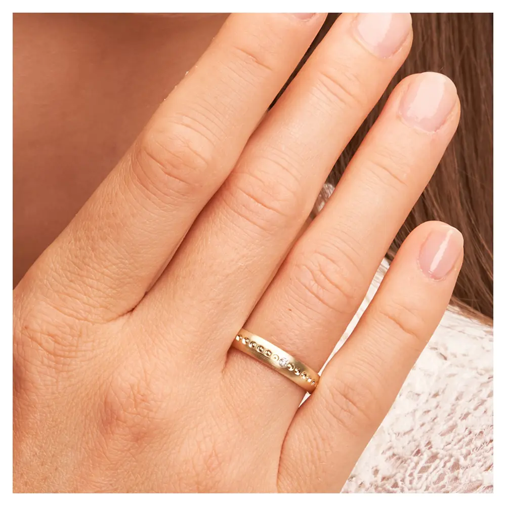 Mattierte Eheringe aus Gelbgold mit Diamanten und Millgriff auf Hand im Zoom