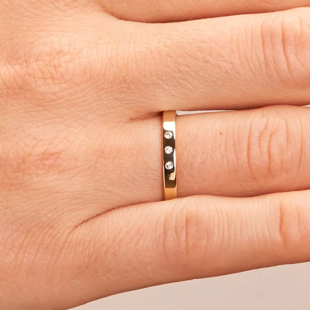 Polierte Eheringe aus Gelbgold mit 3 einzeln gefassten Diamanten auf Hand im Zoom