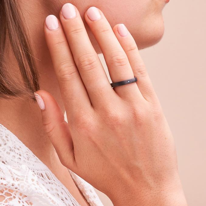 Aufnahme von schmalen schwarzen Eheringen aus Carbon mit blauem Diamanten auf Hand