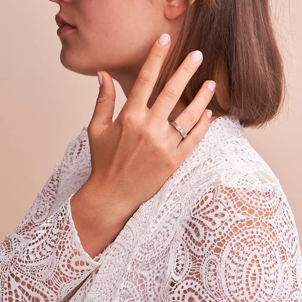 Titan Ehering 4 mm breit mit Mattierung mit Pavee Diamant in Spannfassung auf Hand im Gesicht