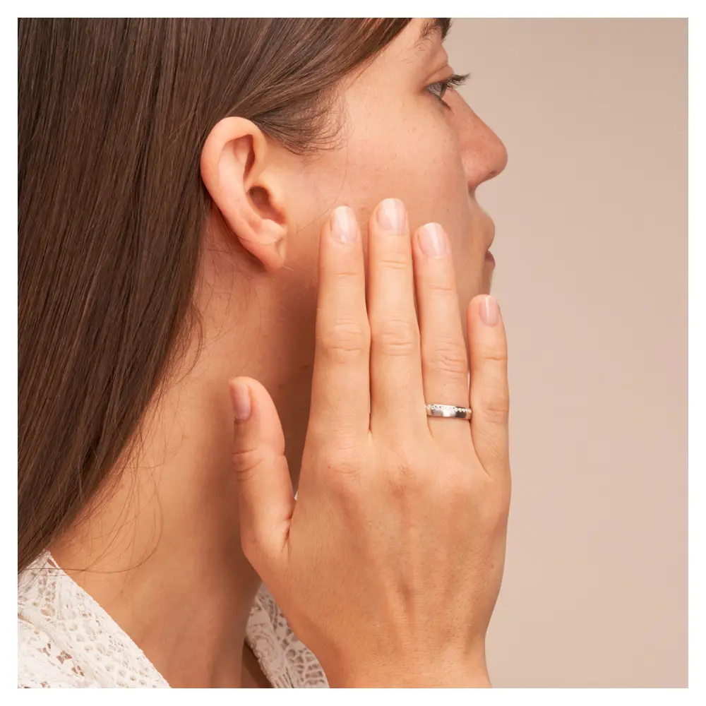 Mattierter Ehering aus rhodiniertem Silber 925 mit Band aus Zirkonia auf Hand am Gesicht