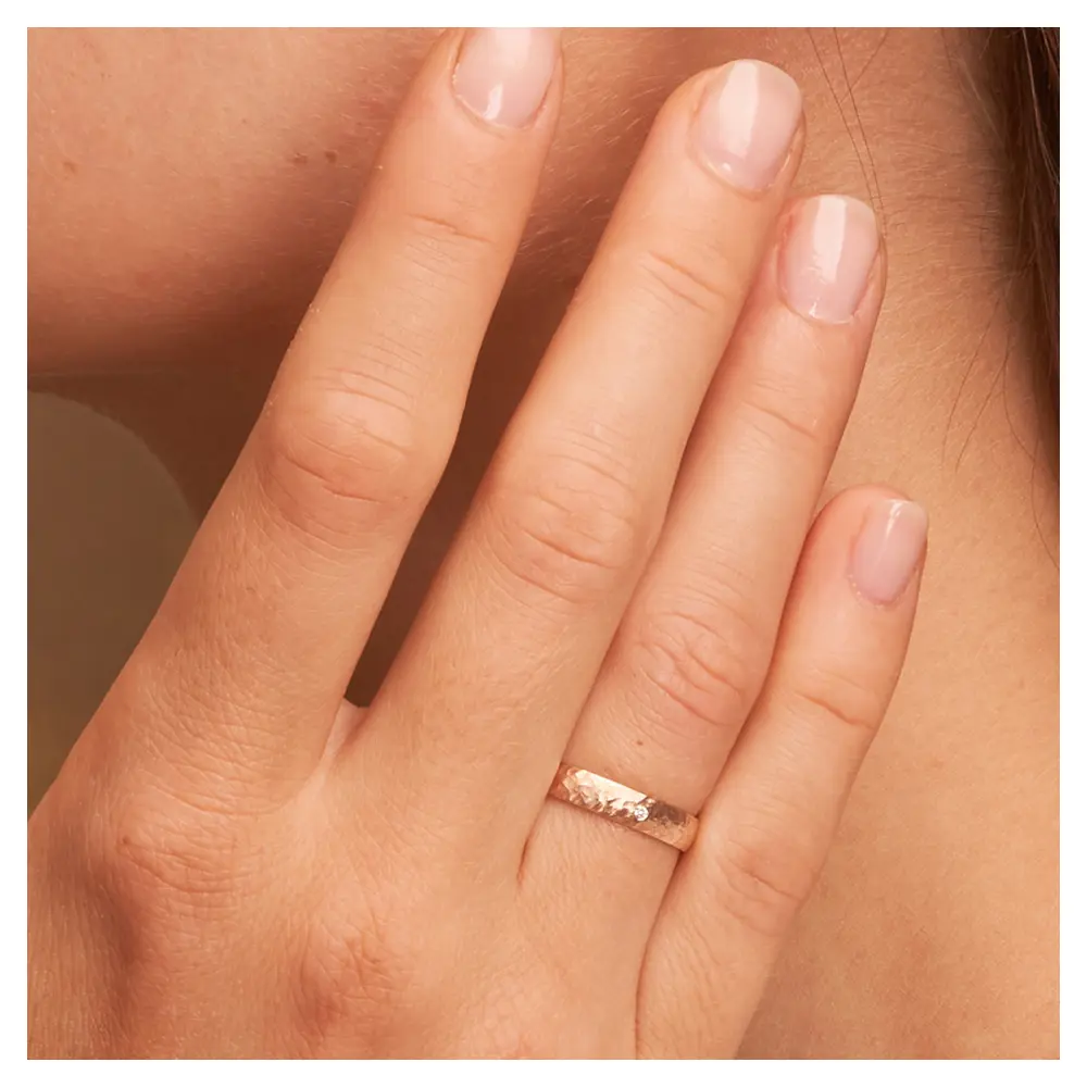 Eheringe aus Roségold mit Hammerschlag und Diamanten auf Hand am Gesicht im Zoom