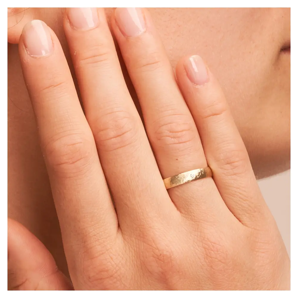 Gelbgold Ehering mit Hammerschlag mit Diamanten auf Hand am Gesicht im Zoom