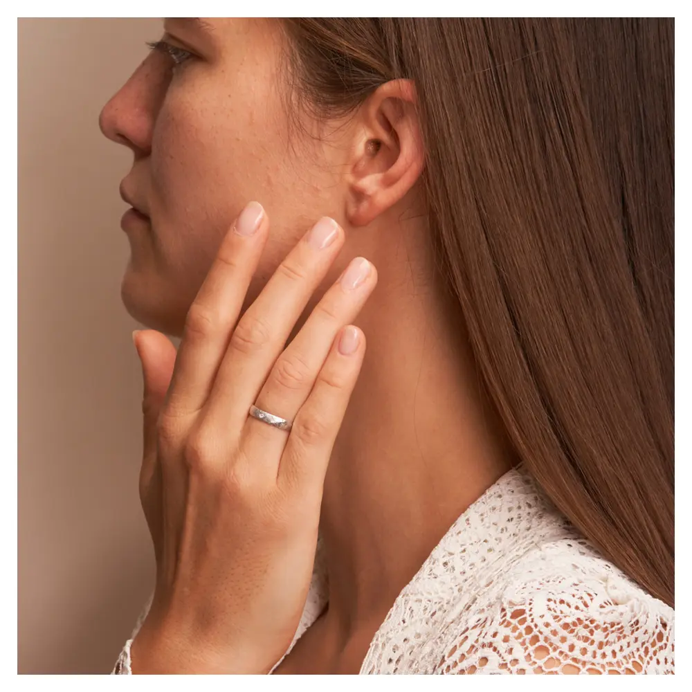 Ehering aus Weissgold in 3 mm mit Hammerschlag und Diamanten auf Hand am Gesicht