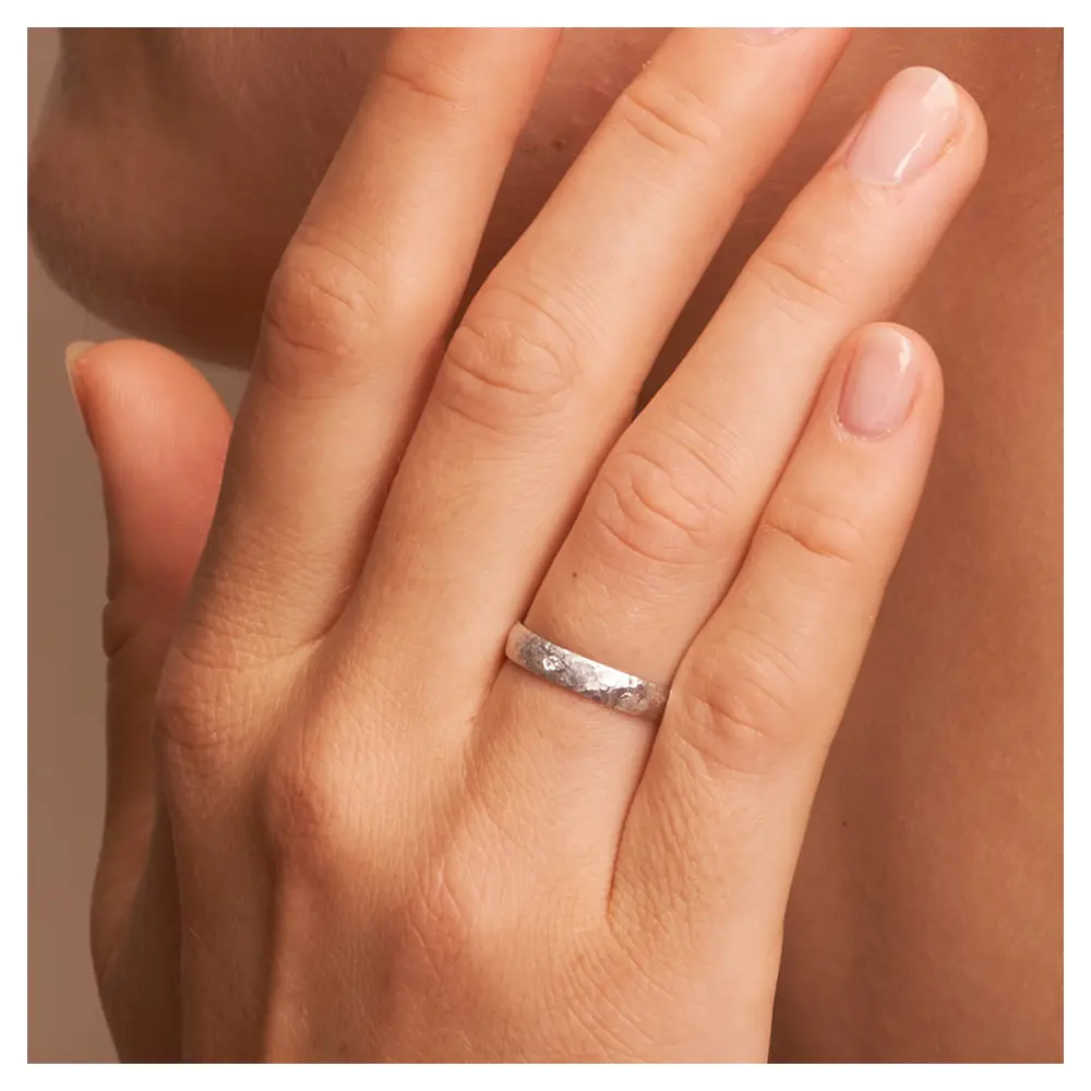 Ehering aus Weissgold in 3 mm mit Hammerschlag und Diamanten auf Hand am Gesicht im Zoom