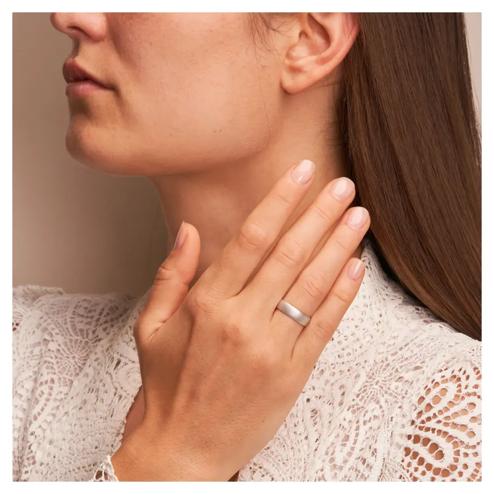 Weissgold Trauring sandmatt mit Diamanten und 5 mm Breite auf Hand am Gesicht