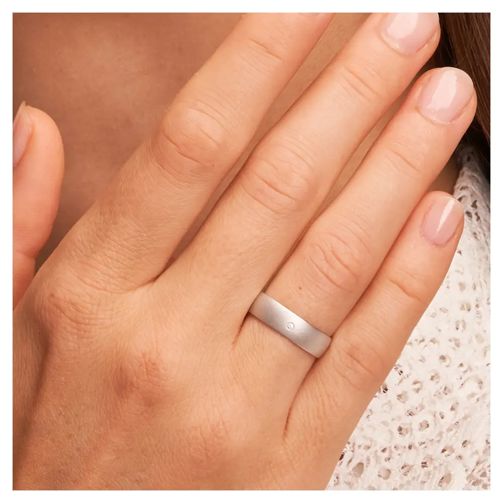 Weissgold Trauring sandmatt mit Diamanten und 5 mm Breite auf Hand am Gesicht im Zoom