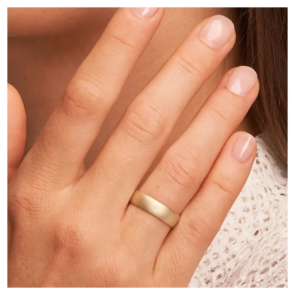 Gelbgold Trauring aus Gelbgold sandmatt mit Diamanten und 5 mm Breite auf Hand am Gesicht im Zoom