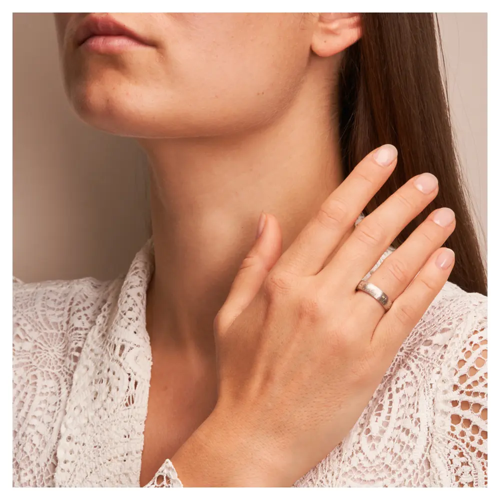 Weißgold Trauring mit Blumen als Dekor und vierzehn Diamanten auf Hand am Gesicht