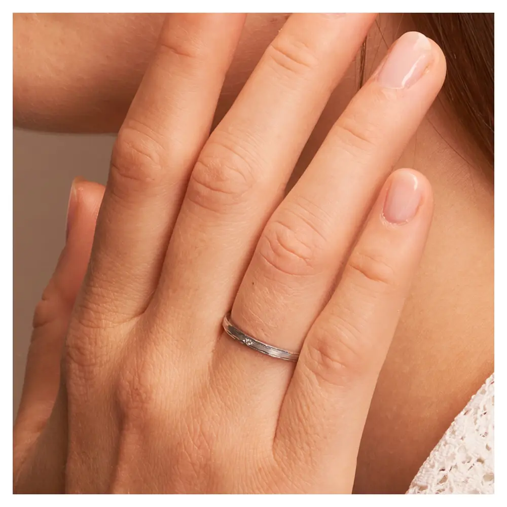 Trauringe Palladium 2 mm breit mit Randmuster und Diamant auf Hand im Zoom