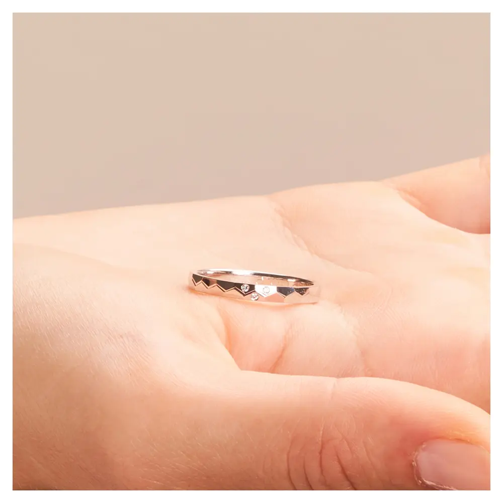 Platin Eheringe mit geometirschem Muster und 3 Diamanten auf Hand liegend