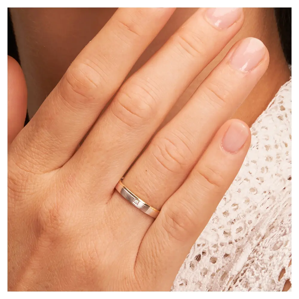 Gelbgold und Weissgold Ehering mit Diamanten und Mattierung auf Hand am Gesicht im Zoom
