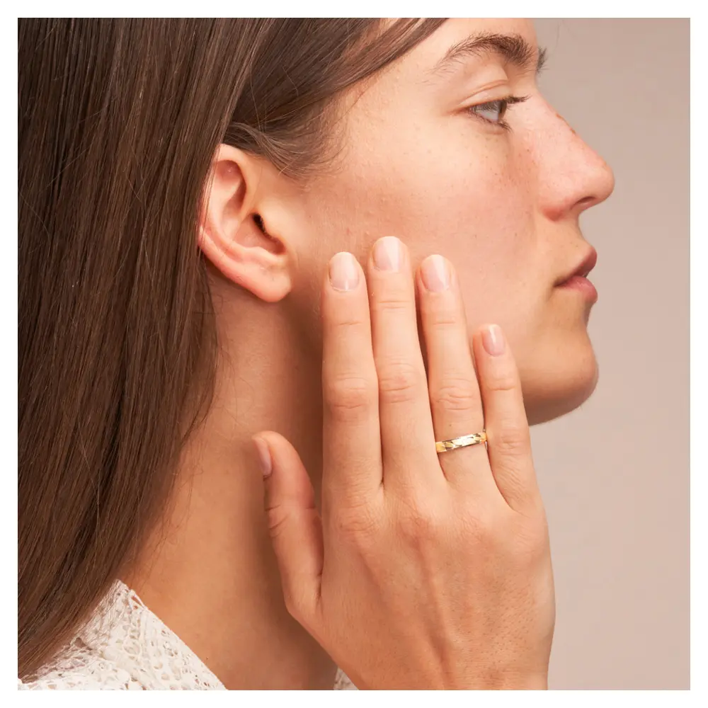 Gelbgold und Weissgold Ehering mit Sichelmustern und Diamant auf Hand am Gesicht