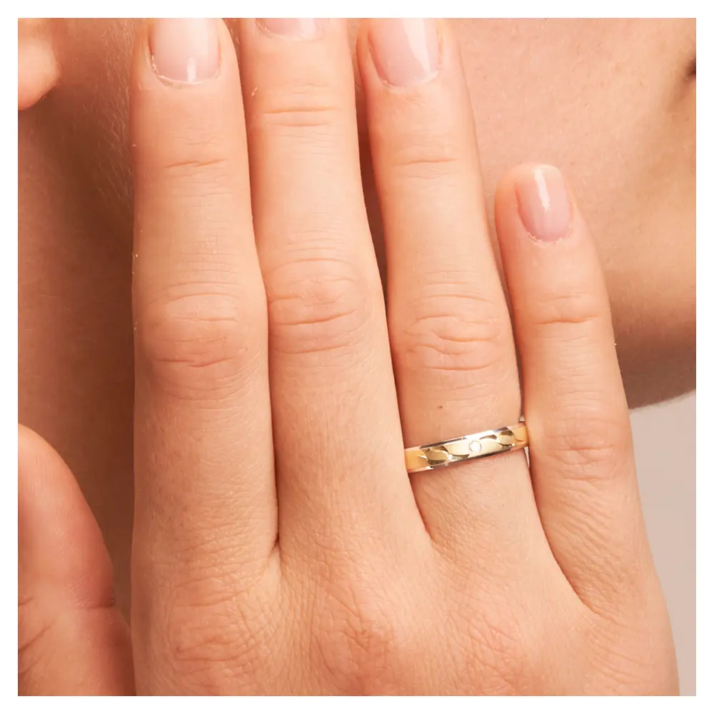 Gelbgold und Weissgold Ehering mit Sichelmustern und Diamant auf Hand am Gesicht im Zoom