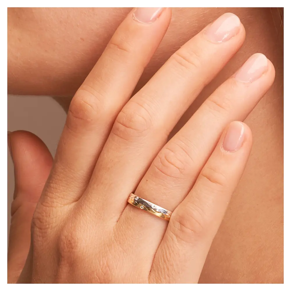 Gelbgold und Weissgold Ehering mit Muster aus Halbmonden und Diamant auf Hand am Gesicht im Zoom
